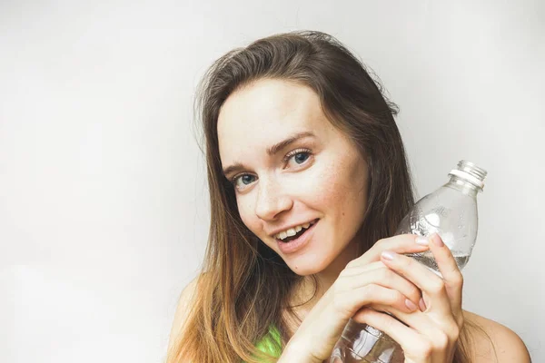 Ganska lysande flicka med flaska vatten, leende, mot vit bakgrund — Stockfoto