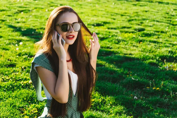 Donna che parla con il cellulare, parla, sorridente.Ragazza in occhiali da sole, intorno all'erba verde — Foto Stock