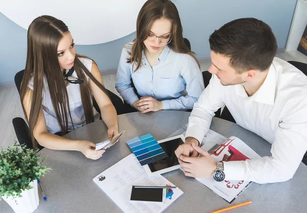 Successful young girls and a guy are sitting at the table in the office, working together on a project — Stock Photo, Image