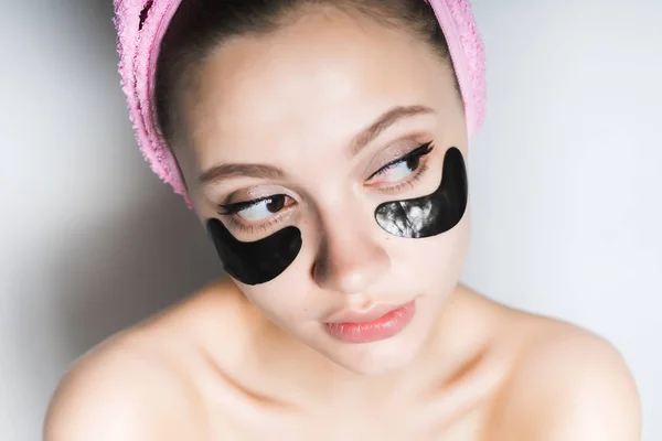 Νεαρό κορίτσι με μαύρο σιλικόνης μπαλώματα κάτω από τα μάτια, με μια ροζ πετσέτα στο κεφάλι της, ψάχνει μακριά — Φωτογραφία Αρχείου