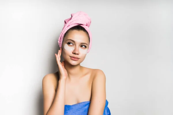 Νεαρό κορίτσι με μια ροζ πετσέτα στο κεφάλι της μοιάζει μετά το πρόσωπό της, σκέφτεται κάτι, αναζητά — Φωτογραφία Αρχείου