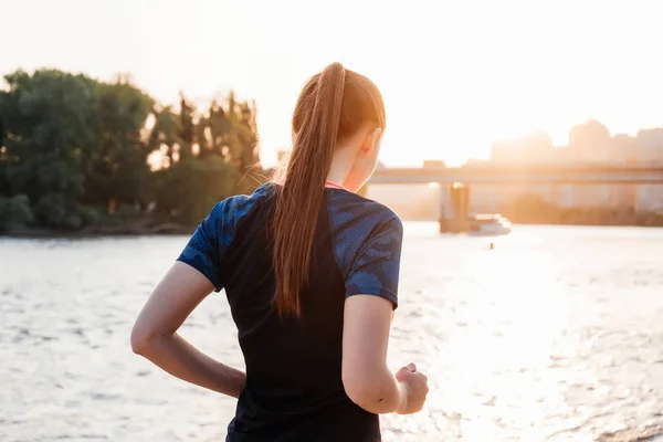 Unga fitness tjej i sportkläder körs vid floden vid solnedgången — Stockfoto