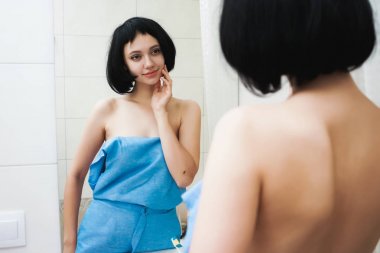 Mavi havlu içinde kısa siyah saçlı güzel genç kız kendini Aynaya bakar