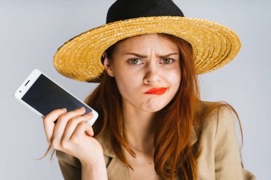 Kırmızı dudaklar ile büyük sesil şapkalı bir kız bir telefon onun elinde tutan ve kameraya memnun seyir