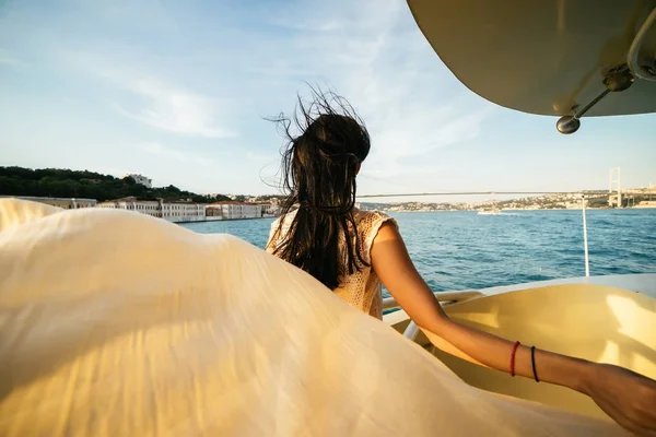 Una ragazza non riconosciuta si trova sul bordo di una barca al tramonto con un fazzoletto, un romantico tramonto a Istanbul, un ponte sullo sfondo — Foto Stock