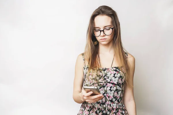 Menina perturbada com celular. menina de cabelos longos com óculos em um vestido bonito olha para o telefone — Fotografia de Stock