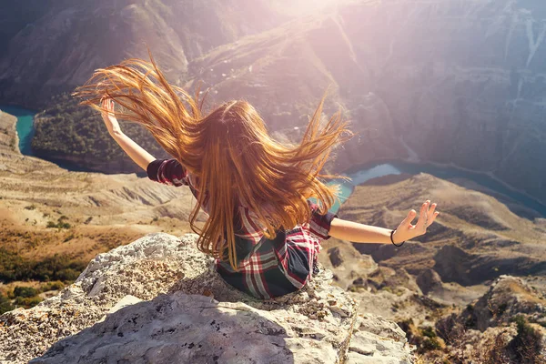 Дівчина має довге красиве волосся, що летить на вітрі. Жінка сидить на краю каменю і дивиться вниз — стокове фото