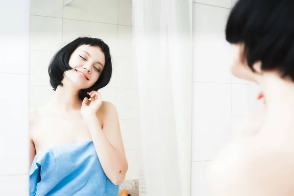 Счастливая девушка с короткими черными волосами смотрит на себя в зеркало — стоковое фото