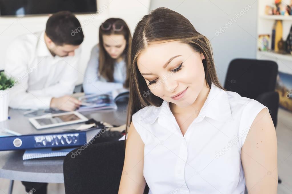 beautiful girl in a white shirt smiles, behind her a man and a girl are working together on a project