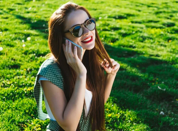 Woman talking with mobile,speaking,smiling.Girl in sunglasses,sitting on green grass — Stock Photo, Image