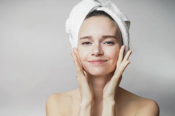 Jovem sorrindo menina com uma toalha branca na cabeça fazendo massagem facial — Fotografia de Stock