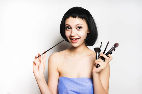 Menina encantadora sorridente com cabelo preto segura em mãos escovas cosméticas pretas — Fotografia de Stock