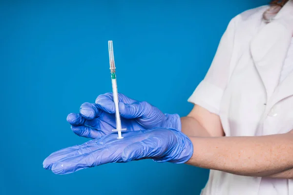 Doctora en bata médica blanca y guantes azules sostiene una jeringa en las manos — Foto de Stock