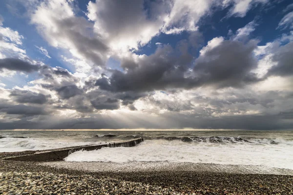 Raging sea near the beach from the pebbles, the sky is covered with gray clouds, the sun is almost invisible — Stock Photo, Image