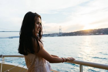 Genç kız gezgin bir yatta seyir ederken rahatlatır, gün batımı ve okyanus bakarak, arka plan üzerinde köprü