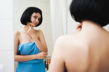 Siyah saçlı, mavi bir havlu ile çekici genç kız kendini ayna ve gülümser görünüyor