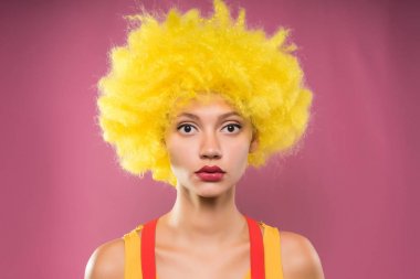 kamera, pembe bir arka plan, sarı palyaço peruk ciddi genç kız bakar