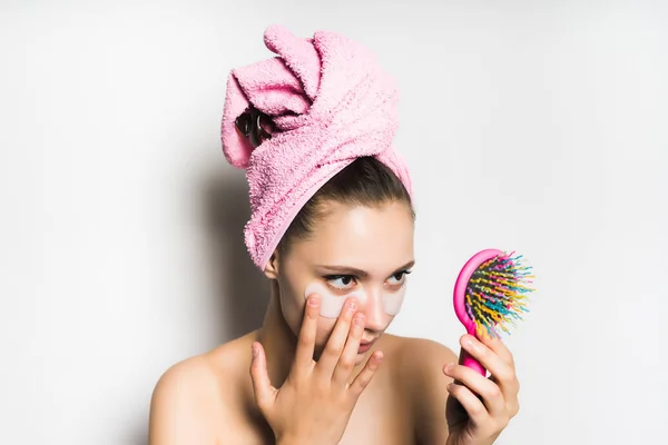 beautiful young girl with a pink towel on her head looking in the mirror, glues silicone patches under the eyes against bruises