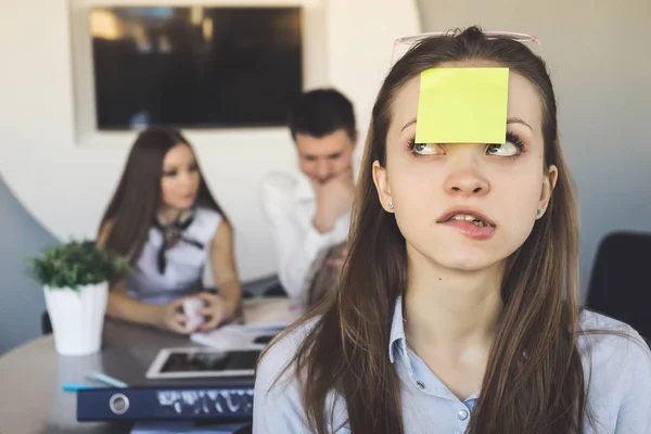 Engraçado jovem trabalhador de escritório menina, folha amarela colada na testa, atrás cara e menina trabalhando juntos — Fotografia de Stock