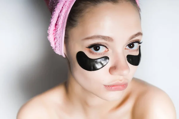Όμορφο κορίτσι με καθαρό δέρμα, κάτω από τα μάτια μαύρα μπαλώματα σιλικόνης, στο κεφάλι μία πετσέτα ροζ — Φωτογραφία Αρχείου