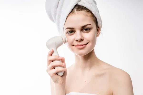 Sorridente ragazza con un asciugamano bianco sulla testa si pulisce il viso con una spazzola elettrica — Foto Stock