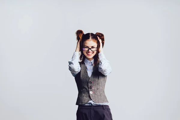 Une jeune écolière drôle avec des lunettes et un gilet gris touche ses cheveux, rit — Photo