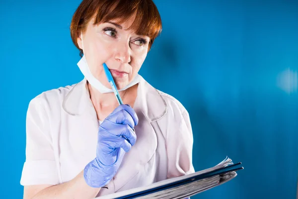 Medico donna adulta in vestaglia medica bianca tiene un notebook e penna nelle sue mani, pensa a qualcosa — Foto Stock