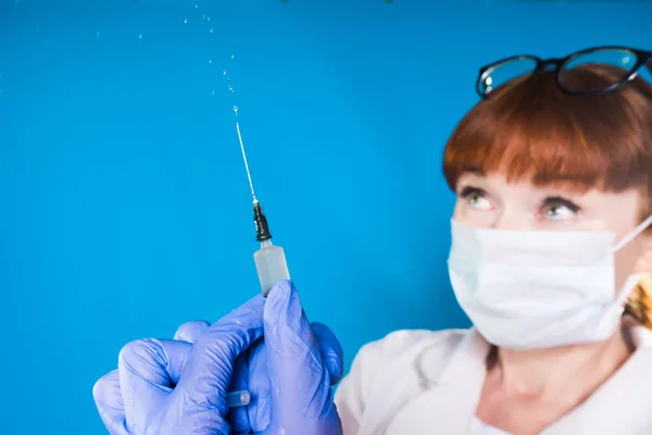 Mujer adulta con bata médica blanca y máscara protectora blanca sostiene la jeringa en las manos — Foto de Stock