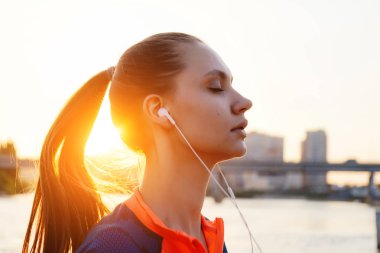Sportif kız kulaklıklar, gün batımında nehrin müzik dinlemek