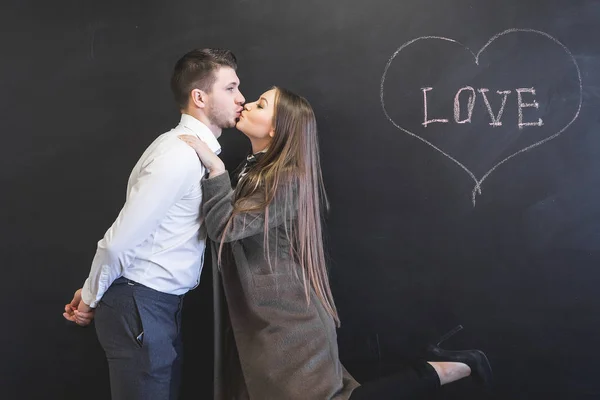 Jeune couple amoureux embrasser sur un fond de tableau sur lequel le mot amour est écrit — Photo