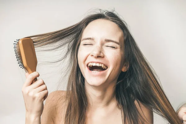 Mujer feliz peinando pelos con peine, ríe, sobre un fondo blanco —  Fotos de Stock