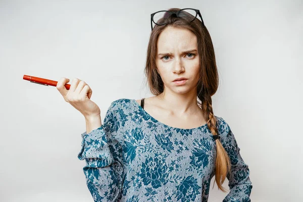 Грустная сердитая молодая девушка в очках и в модной куртке держит ручку в руке — стоковое фото