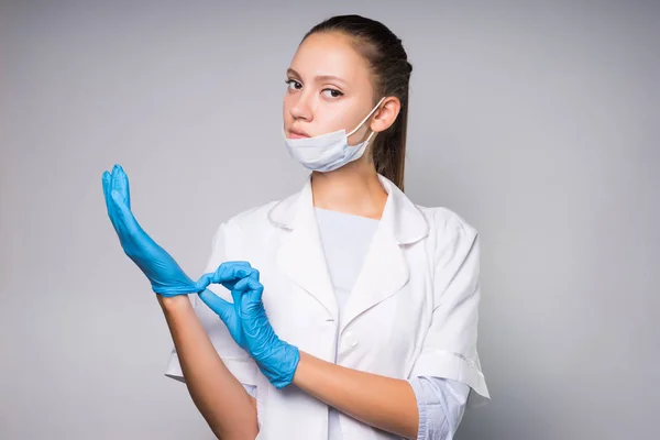 파란색 장갑에 흰색 보호 의료 마스크, 드레싱 가운, 심각한 젊은 여자 의사 — 스톡 사진