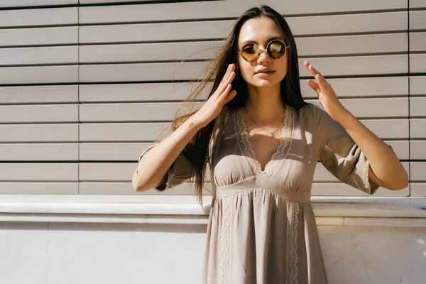 Attractive sexy girl with long hair wearing sunglasses in a beige dress posing in the sun — Stock Photo, Image