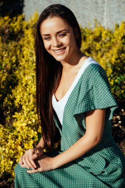 Gülümseyen şık yeşil elbiseli, sarı arka plana sahip büyüleyici doğal kadın