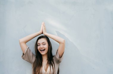 uzun saçları hafif bir duvarın ardında, poz mutlu gülen kız Eller yukarı doğru kaldırdı