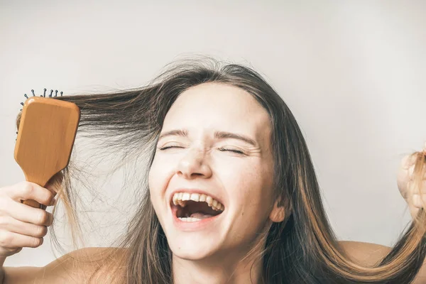 Забавный счастливый подросток наслаждается здоровыми волосами, расчесывает волосы деревянной расческой — стоковое фото