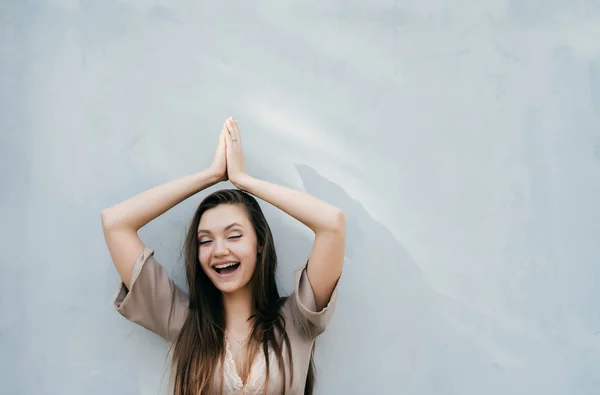 Happy smějící se dívka s dlouhými vlasy představují světle zdí, ruce zvedl nahoru — Stock fotografie