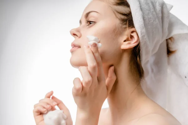 Young girl with a white towel on her head applying a nourishing cream on her face — Stock Photo, Image