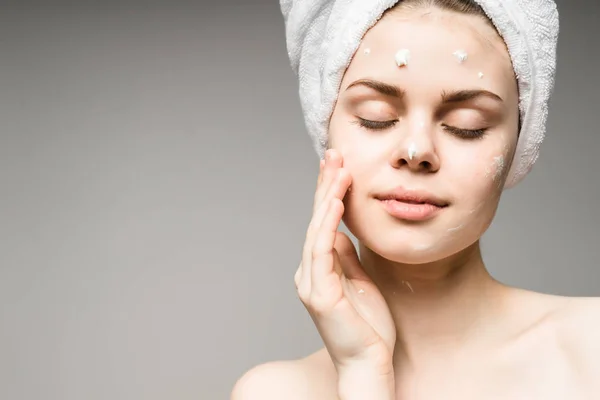 A girl with a towel on her head closing her eyes puts a cream on her face — Stock Photo, Image