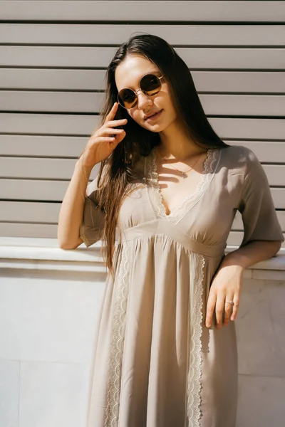 A lány nyári ruhák és napszemüveg hajlik a falhoz, az utcán — Stock Fotó
