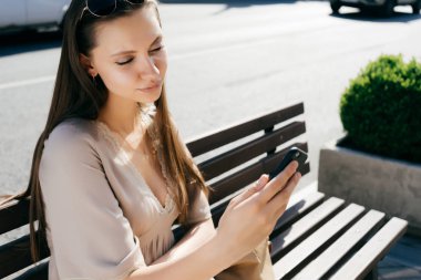güzel kız sokak şehirde bir bankta oturur ve selfie yapar. sıcak güneşli