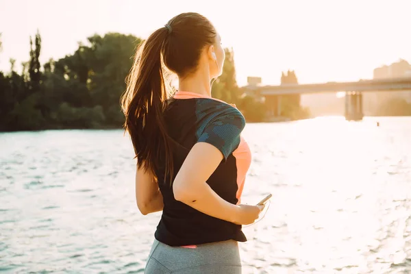 Sport långhåriga flicka springer runt floden i solen, lyssnar på musik i hörlurar — Stockfoto