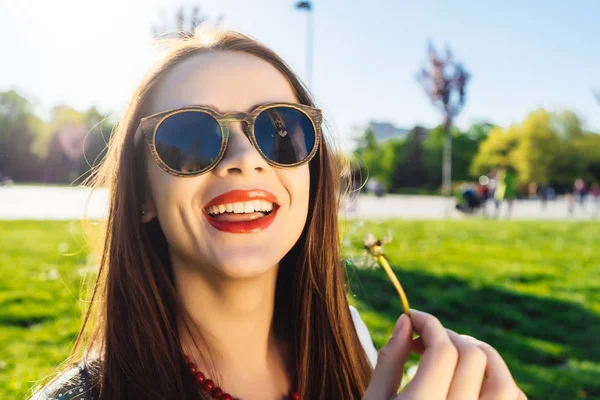 Divertente sorridente donna felice in occhiali da sole che soffia dente di leone — Foto Stock