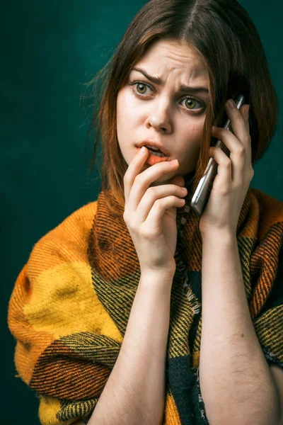Uma menina assustada envolto em um lenço quente e falando com alguém no telefone, isolado em um fundo verde — Fotografia de Stock