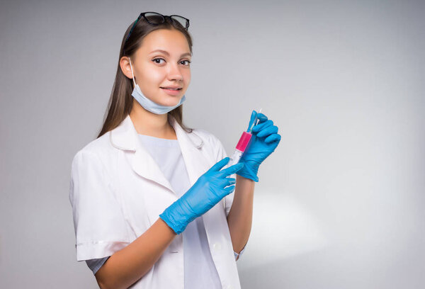 the girl in a medical gown and gloves holds a syringe in her hands and looks smilingly at the camera