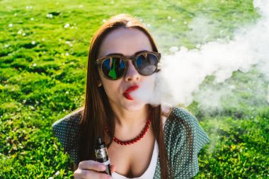 Mutlu moda gülümseyen kadın güneş gözlüğü vape Street, duman Sigara