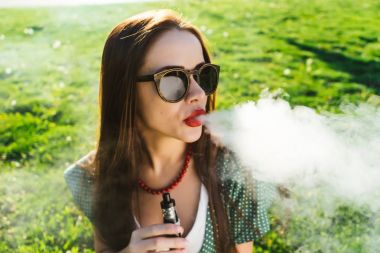 Mutlu moda gülümseyen kadın güneş gözlüğü vape Street, duman Sigara
