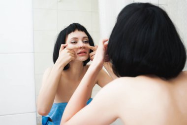 Mavi havlu içinde kısa siyah saçlı güzel genç kız kendini Aynaya bakar ve onun yüzünü temizler