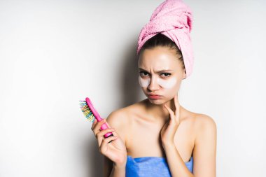 onun baş ve silikon yamalar bir tarak onun elinde tutarak gözlerinin altındaki pembe havlu ile üzgün genç kız